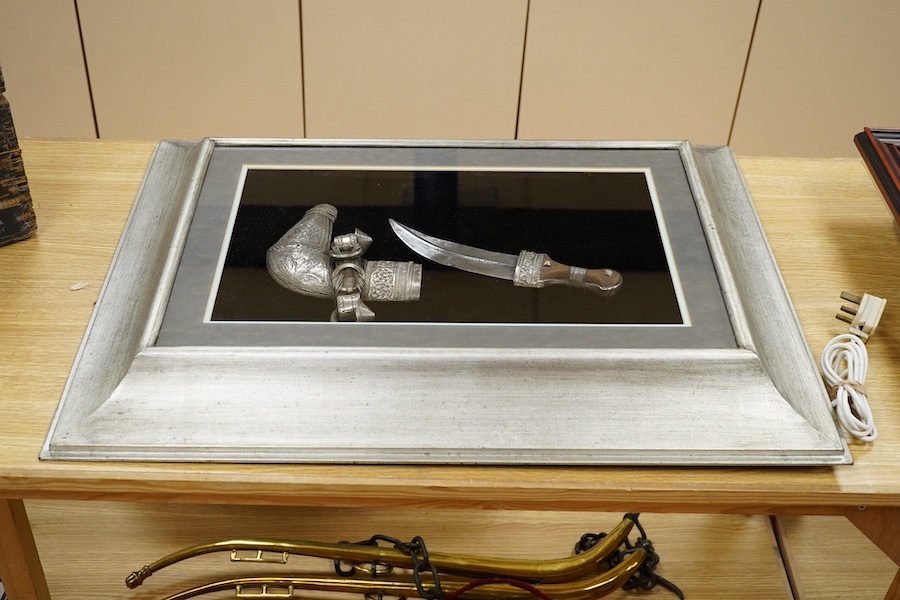 A silver mounted Arab Khanjar dagger from Oman, wooden grip, mounts chased in relief with scrolling foliage, contained in an illuminated display case for wall mounting, 79cm x 58.5cm. Condition - good.